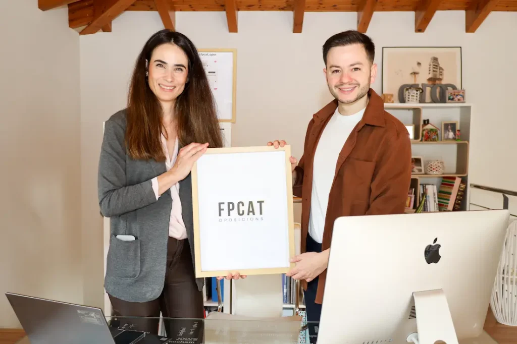 Doli i Alberto, de FpCat Oposicions, amb el cartell de FpCat